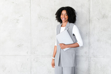 Exuding professionalism, an African-American woman stands confidently with a laptop in hand,...