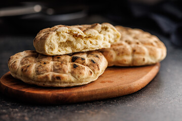 Arabic flat pita bread on cutting board on black table.