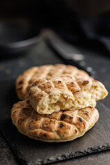 Arabic flat pita bread on cutting board on black table.