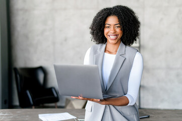 A vibrant African-American businesswoman with a laptop, her beaming smile portraying confidence and digital competence in minimalist office setting. A dynamic professional engaged in the digital world