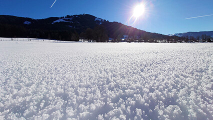 Snow textures after fresh snowfall, forming ice crystals on the ground and beautifull untouched snow cover. In the background, underneath a beautifull blue and sunny sky, the mountains of Westendorf.
