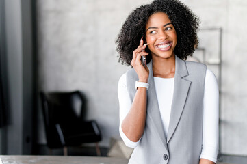 With a radiant smile, an African-American businesswoman converses on her phone, effortlessly...