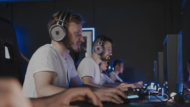 Bristly gamers playing video game on PC at computer club, cyber sport tournament. E-sport team at championship. Five players in headset. Multiplayer online first-person shooter, real-time strategy RTS
