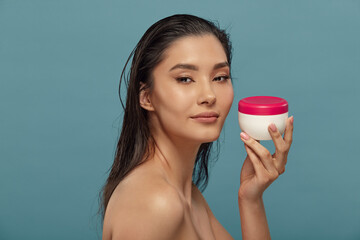 Headshot portrait of asian girl holding round cream jar.