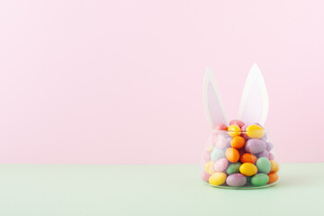 Colorful candy jar decorated with bunny ears against pink background, gifts for Easter