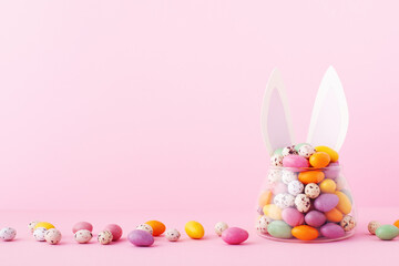 Colorful candy jar decorated with bunny ears against pink background, gifts for Easter