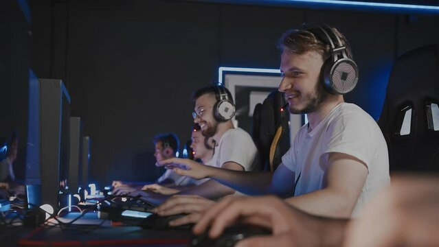 Bristly gamers playing video game on PC at computer club, cyber sport tournament. E-sport team at championship. Five players in headset. Multiplayer online first-person shooter, real-time strategy RTS