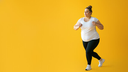 A graceful dancer in a flowing white shirt and active pants leaps off a yellow wall, showcasing her physical fitness and passion for movement