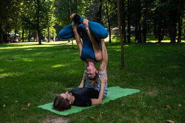 Boy and girl doing acro yoga outdoors in summer in public park