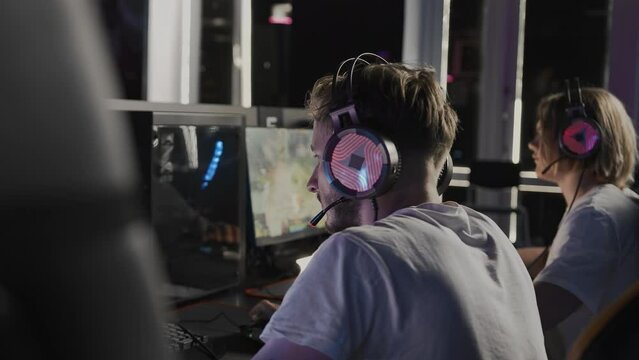 Bristly adult gamer in headset plays a video game on PC at computer club, cyber sport tournament. E-sport championship. Players team. Multiplayer online battle competition, PvP real-time strategy RTS