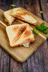 Toasted sandwich with  ham, cheese and basil  served on wooden cutting board