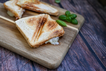 Toasted sandwich with  ham, cheese and basil  served on wooden cutting board