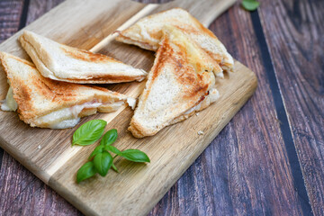 Toasted sandwich with  ham, cheese and basil  served on wooden cutting board