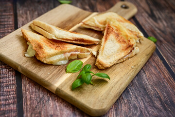 Toasted sandwich with  ham, cheese and basil  served on wooden cutting board