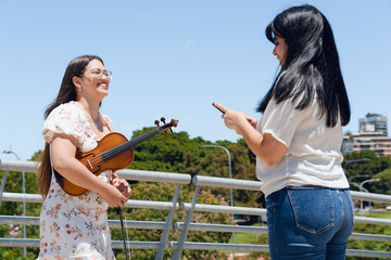 young latina busker violinist woman giving her phone number to tourist outdoors.