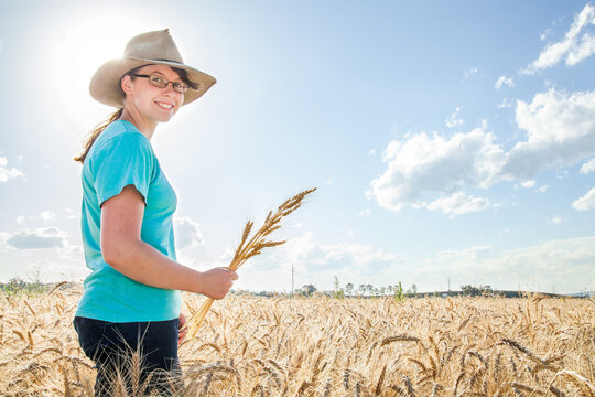 Sunflare behind a happy farm girl holding a sheaf of bearded wheat