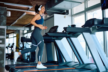 Fototapeta na wymiar Full length of happy sportswoman jogging on treadmill in health club.