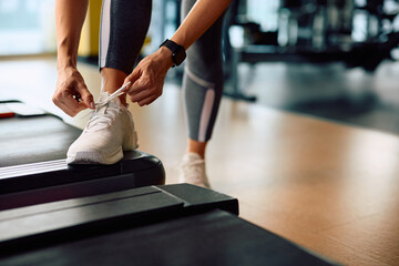 Close up of athletic woman tying shoelace while exercising in health club. - obrazy, fototapety, plakaty