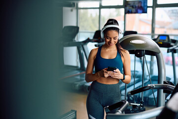 Happy sportswoman texting on cell phone while working out in gym.