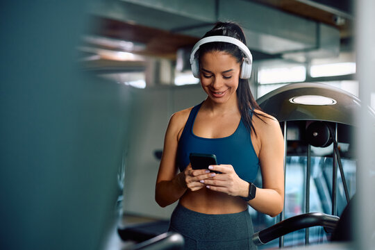 Happy athletic woman listening music over headphones while using mobile phone during gym workout. - Powered by Adobe