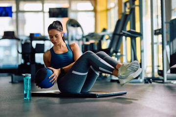 Fototapeta na wymiar Young athletic woman using medicine ball while doing sit-ups during sports training in gym.