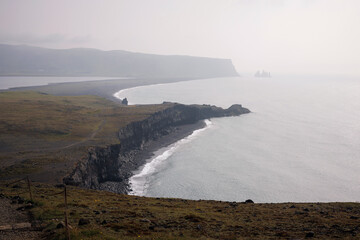 Iconic scenery of Reynisfjara beach in Iceland, beautiful coastline with black volcanic sand, basalt cliff, and rocks in the Atlantic Ocean, aerial view.