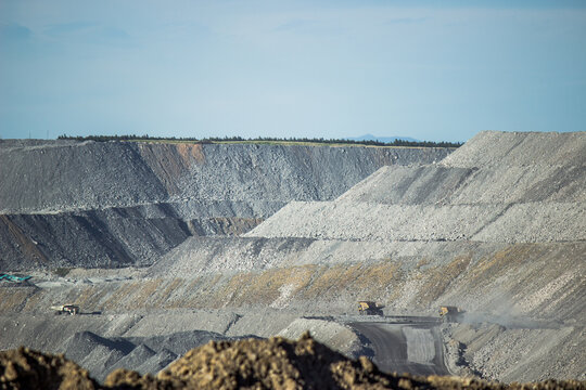 Distant dump trucks carting coal in grey hills of open cut mine