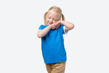 Cute little girl in a blue t-shirt covering her face with her hands and pretending to sleep,...