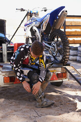 Motorbike, race and sports with man getting ready for off road adrenaline, competition or training outdoor. Boots, adventure and dirtbike hobby with person in gear on trailer for performance