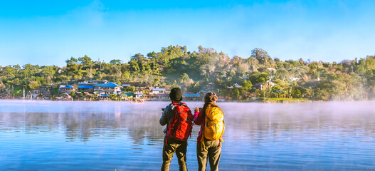Asian woman and Asian man which backpacking standing near the lake, she was smiling, happy and...