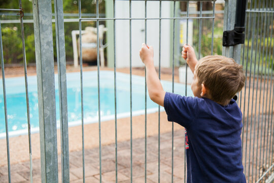 Young boy outside pool fence looking in to pool yard