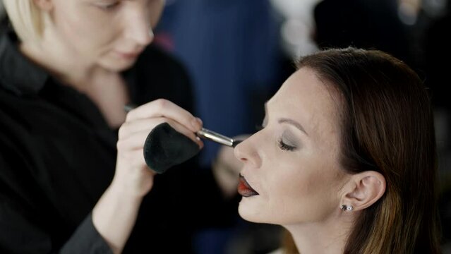 makeup artist gay and beautiful middle-aged model woman in beauty studio, preparing to fashion show