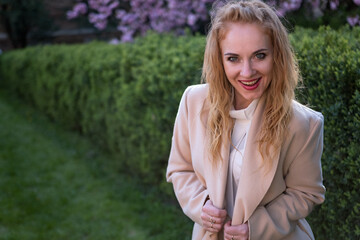 Portrait of ginger-tressed beauty in beige coat in park smiling and looking at the camera. Girl with crazy look.