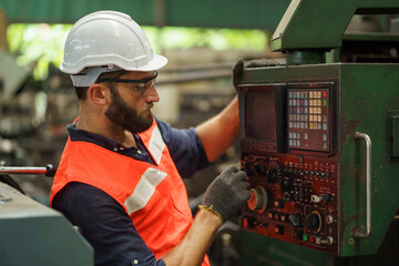 caucasian industrial worker beard man with helmet controlling cnc machine or maintenance in...