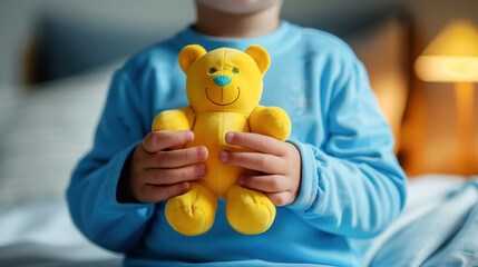 A child in blue pajamas sits on his crib and holds a yellow teddy bear. Child health concept, caring for special children, World Autism Awareness Day