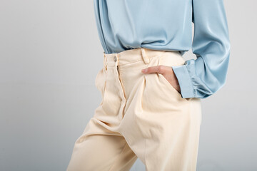 Elegant woman in pleated beige pants and blue blouse with hand in pocket
