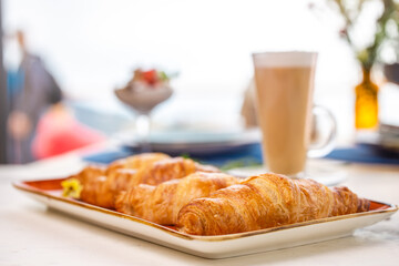 Four golden croissants on an orange plate with a cup of coffee on the side