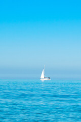Obraz premium white sailboat on the open sea near the horizon against a cloudless sky. Boat trip. place for text