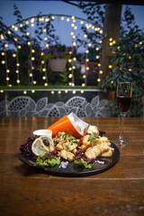 Delicious fried calamari, potatoes, and lemon wedges on a plate with red wine