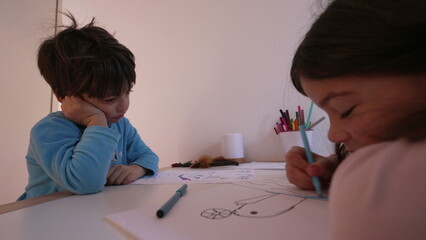 Bored little boy watching sister draw, authentic upset sibling feeling annoyed and boredom