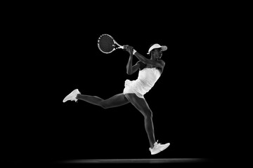 Focused athlete in tennis gear executing powerful forehand swing against black studio background....