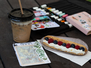 Obraz na płótnie Canvas Artistic workspace with colorful watercolor palette, chalks, coffee, and berry tart on rustic table, with vintage map and plant stickers