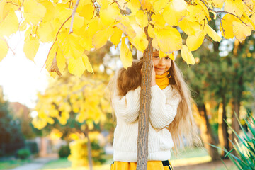 Little girl hiding behind a tree. Happy child on the walk in autumn park.