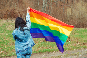 Woman holding the rainbow flag on the nature. Happiness, freedom and love concept for same sex couples. Lifestyle, people and love.