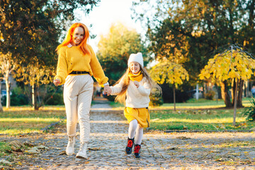 Happy family enjoying autumn weather in the park. Lovely girl with her mom having fun on the walk.