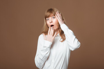 Middle-Aged Woman with Open Mouth and Hand Clasping Her Head in Astonishment, Depicting Astonishment, Reaction to Unexpected News, and Emotional Overload