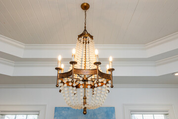 An ornate beaded chandelier light fixture with glowing lit candle type bulbs against a double tray white ceiling