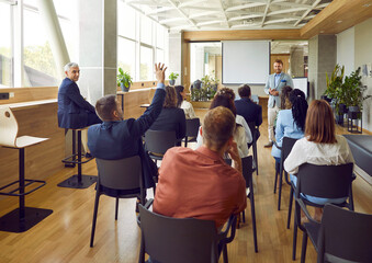 Man raising hand to ask or answer a question on a business meeting. Group of company employees or a...