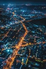 Fototapeta premium The aerial view shows a city at night with bright lights illuminating the urban landscape. Skyscrapers, streets, and buildings are visible, creating a striking contrast against the dark sky