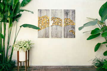 Bali style molding wooden art on white wall, surrounded by many green plants